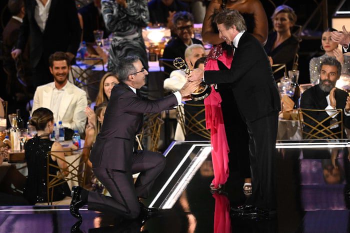 John Oliver si inginocchia mentre accetta il premio per la migliore serie di discorsi di varietà.