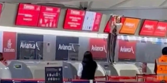 Gli altri passeggeri in aeroporto possono vedere la persona fuori controllo - in piedi al banco del check-in e con uno schermo sopra di essa - da lontano.